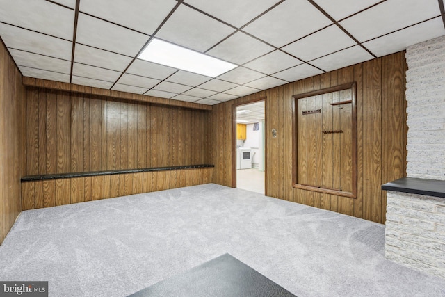 below grade area featuring a paneled ceiling, wooden walls, and carpet flooring