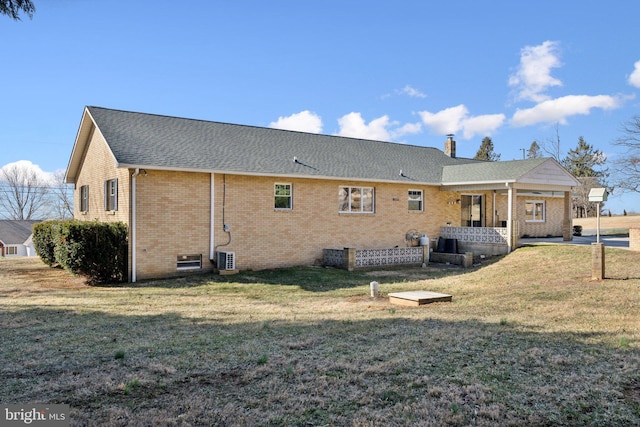 back of house with a yard, brick siding, a chimney, and a shingled roof