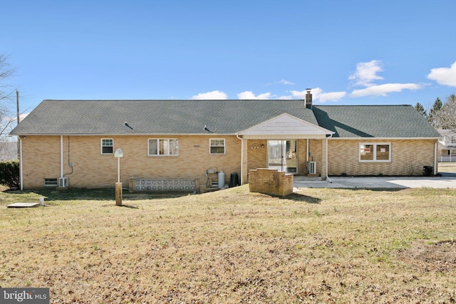 rear view of property featuring a patio area, a lawn, brick siding, and a chimney