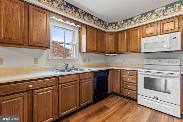 kitchen featuring brown cabinets, light countertops, a sink, wood finished floors, and white appliances