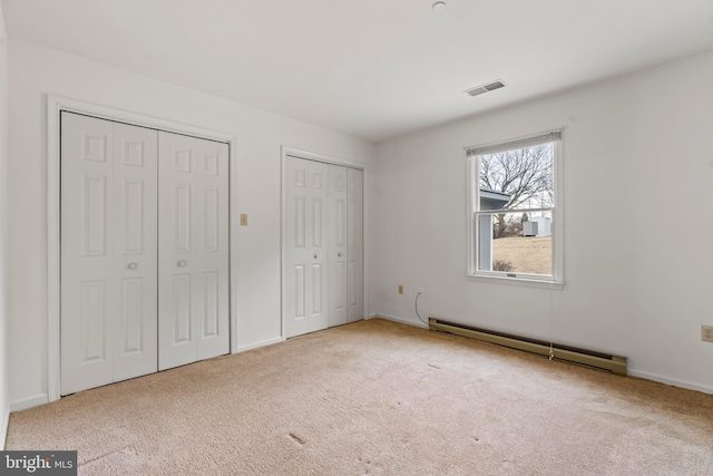 unfurnished bedroom with two closets, visible vents, baseboard heating, carpet flooring, and baseboards