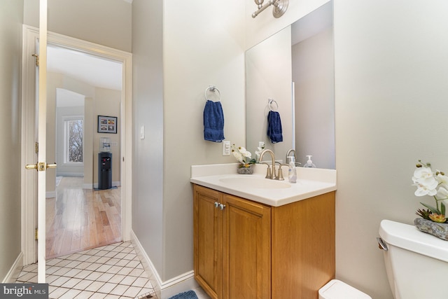 half bathroom with toilet, tile patterned floors, baseboards, and vanity