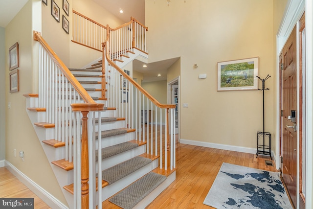 foyer entrance featuring a towering ceiling, hardwood / wood-style flooring, stairway, and baseboards