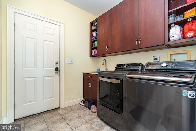 clothes washing area featuring cabinet space, baseboards, washing machine and clothes dryer, a sink, and light tile patterned flooring