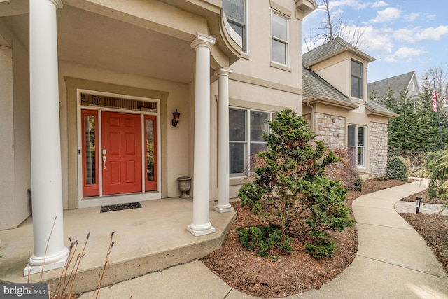 entrance to property featuring stone siding, a shingled roof, and stucco siding