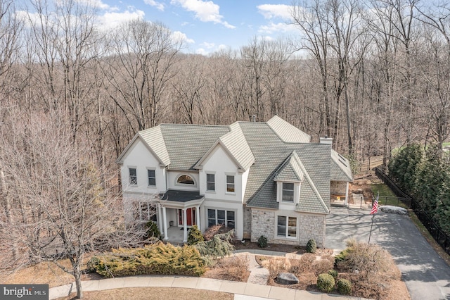 view of front of property featuring aphalt driveway, a tile roof, a chimney, a wooded view, and stone siding