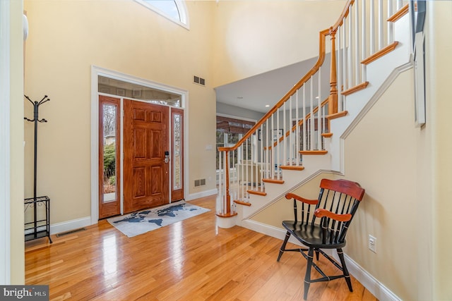 foyer featuring visible vents, a towering ceiling, baseboards, and hardwood / wood-style flooring