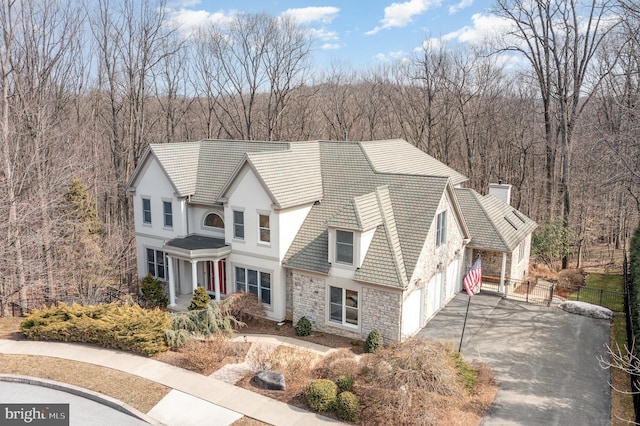 view of front of house with stone siding, aphalt driveway, fence, a wooded view, and stucco siding