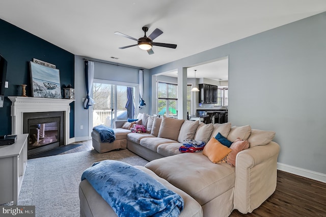 living area featuring visible vents, a fireplace with flush hearth, wood finished floors, baseboards, and ceiling fan