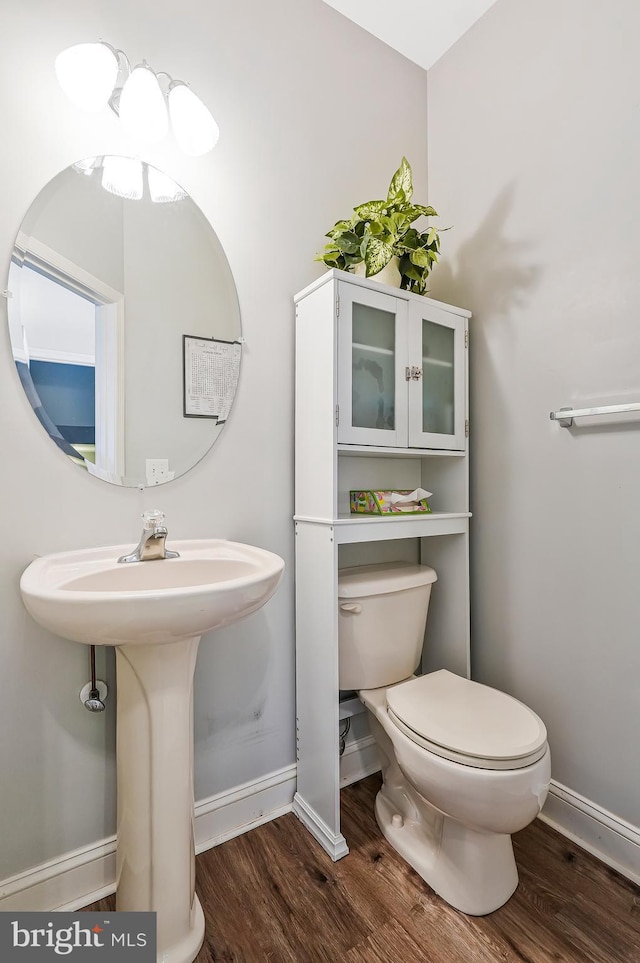 half bathroom with baseboards, toilet, and wood finished floors