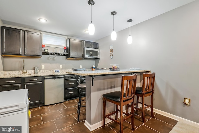 kitchen featuring stainless steel microwave, decorative light fixtures, dishwashing machine, a kitchen breakfast bar, and dark tile patterned flooring