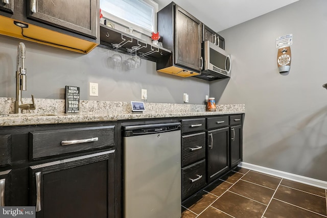 kitchen featuring dark tile patterned floors, light stone countertops, baseboards, and stainless steel appliances