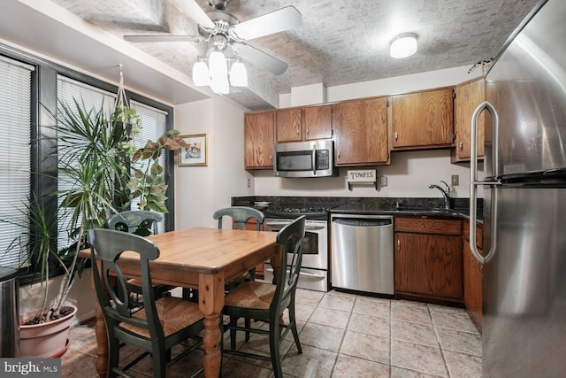 kitchen featuring light tile patterned floors, brown cabinetry, stainless steel appliances, a textured ceiling, and a sink