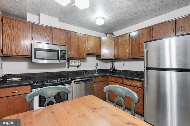 kitchen with appliances with stainless steel finishes, brown cabinetry, and a sink