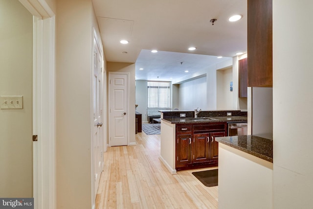 kitchen with dark stone counters, recessed lighting, light wood finished floors, and a sink