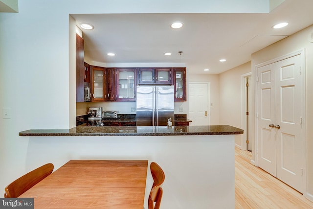 kitchen featuring dark stone countertops, recessed lighting, stainless steel appliances, a peninsula, and light wood finished floors