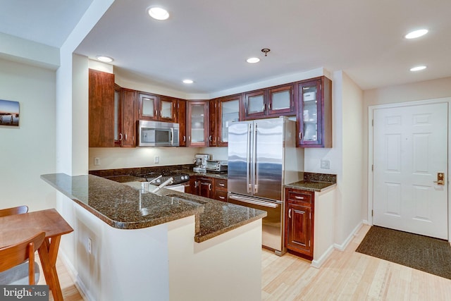 kitchen featuring dark stone countertops, a peninsula, light wood-style flooring, a sink, and stainless steel appliances