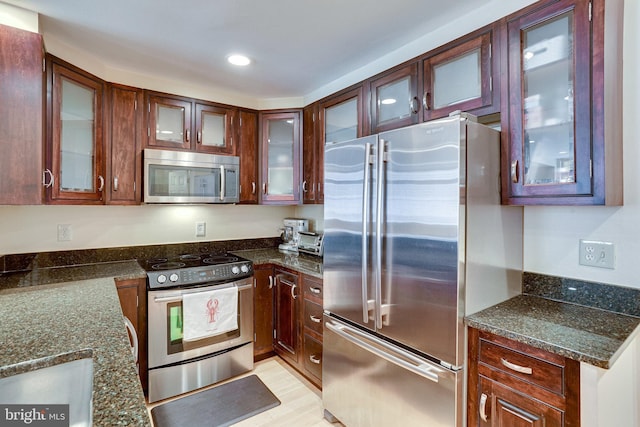 kitchen featuring glass insert cabinets, dark stone counters, light wood-type flooring, recessed lighting, and stainless steel appliances