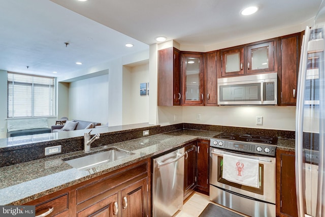 kitchen with dark stone counters, a sink, glass insert cabinets, appliances with stainless steel finishes, and open floor plan