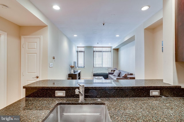 kitchen with recessed lighting, dark stone countertops, open floor plan, and a sink