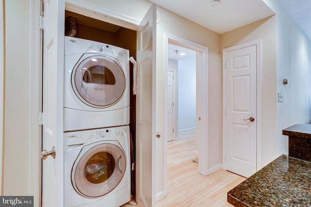 laundry area featuring light wood-type flooring, baseboards, stacked washer and dryer, and laundry area