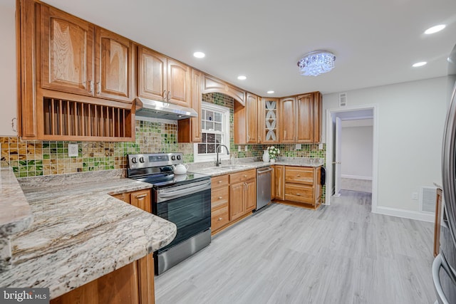 kitchen featuring stainless steel appliances, tasteful backsplash, light wood-style flooring, light stone countertops, and under cabinet range hood