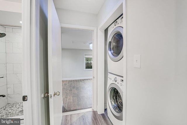 washroom with stacked washing maching and dryer, baseboards, laundry area, and wood finished floors