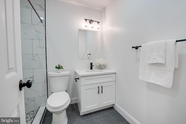 bathroom featuring toilet, tiled shower, vanity, and baseboards