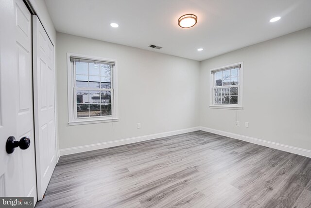 unfurnished bedroom featuring a closet, multiple windows, baseboards, and wood finished floors