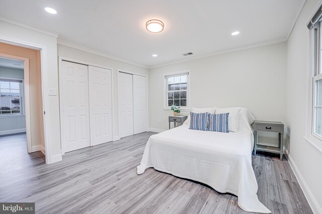 bedroom featuring crown molding, wood finished floors, visible vents, and multiple closets