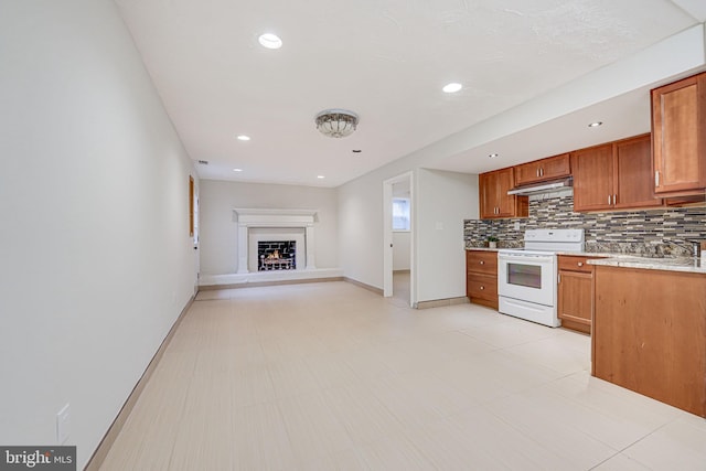 kitchen with a lit fireplace, light countertops, backsplash, brown cabinetry, and white electric range oven