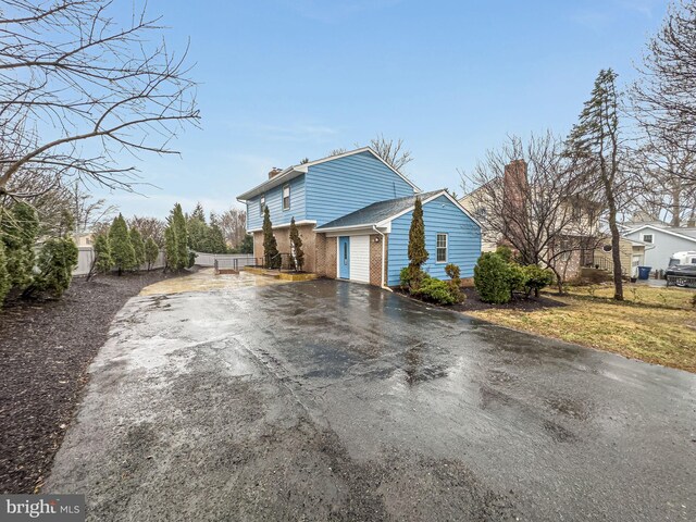 view of property exterior with driveway, brick siding, a chimney, and fence