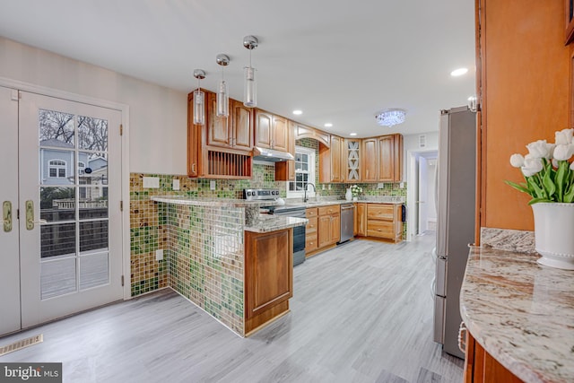 kitchen with light wood-style flooring, appliances with stainless steel finishes, a peninsula, light stone countertops, and under cabinet range hood