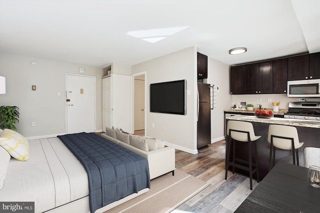 bedroom with light wood finished floors, freestanding refrigerator, and baseboards