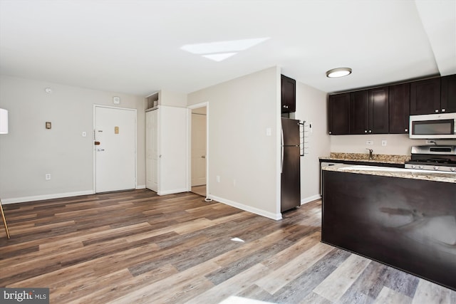 kitchen with stainless steel appliances, light wood-style floors, a sink, dark brown cabinets, and baseboards