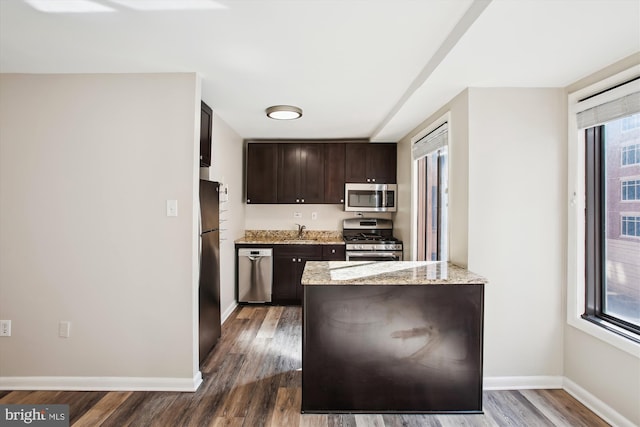 kitchen featuring stainless steel appliances, wood finished floors, a sink, dark brown cabinets, and light stone countertops