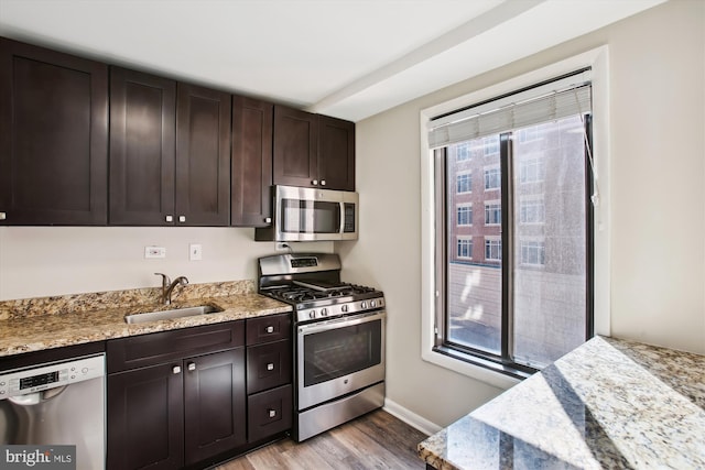 kitchen featuring light wood-style flooring, dark brown cabinetry, stainless steel appliances, a sink, and light stone countertops