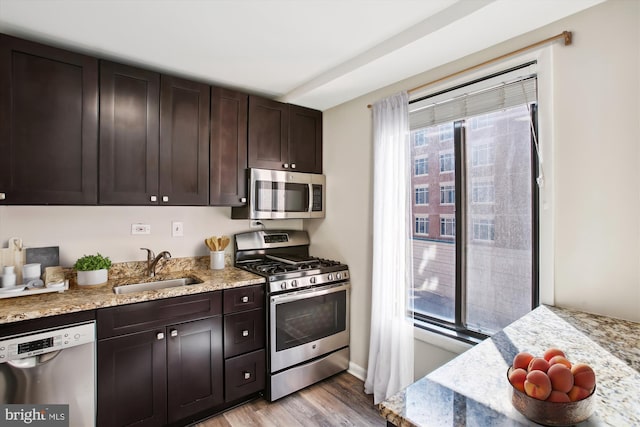 kitchen with light stone counters, stainless steel appliances, a sink, light wood-style floors, and dark brown cabinets