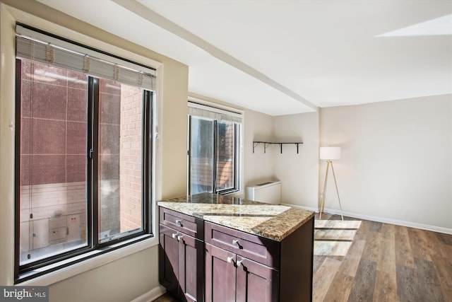 kitchen with light stone countertops, dark brown cabinets, wood finished floors, a peninsula, and baseboards