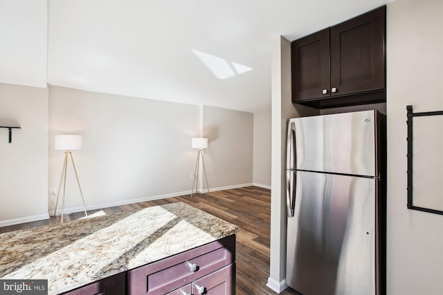 kitchen featuring light stone counters, dark wood-type flooring, baseboards, dark brown cabinets, and freestanding refrigerator