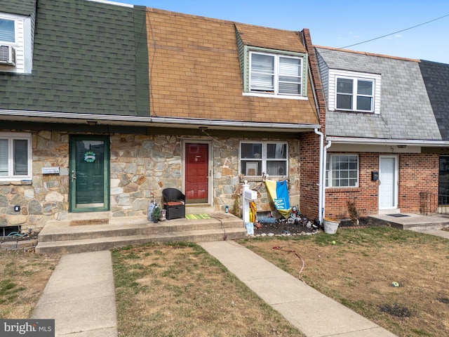 multi unit property with a shingled roof, stone siding, and a front lawn