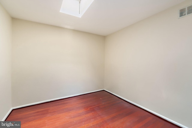 spare room with a skylight, visible vents, baseboards, and hardwood / wood-style flooring