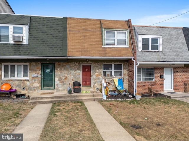 multi unit property featuring stone siding, roof with shingles, and a front yard