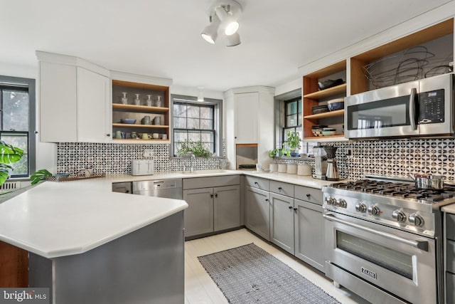 kitchen featuring open shelves, stainless steel appliances, a sink, and gray cabinetry