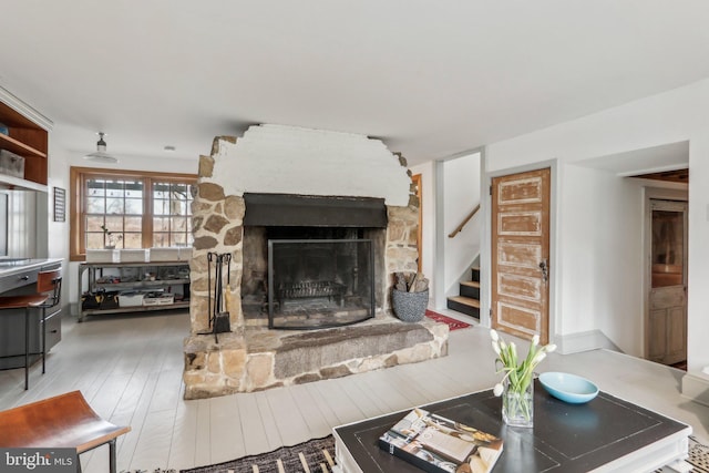 living room with stairs, a stone fireplace, and wood finished floors