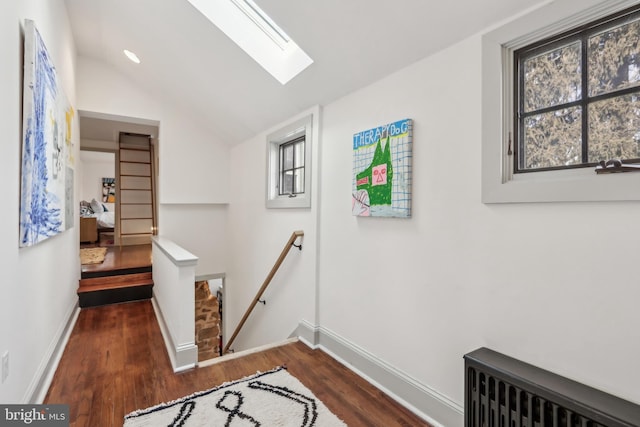 corridor with baseboards, lofted ceiling with skylight, radiator heating unit, dark wood-type flooring, and an upstairs landing