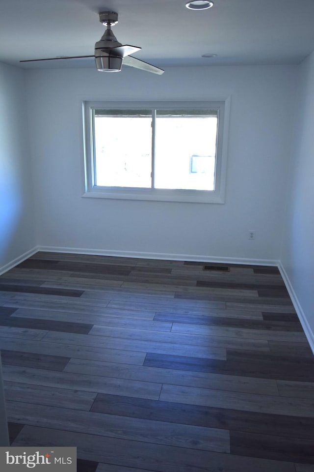 unfurnished room with dark wood-style floors, a ceiling fan, visible vents, and baseboards