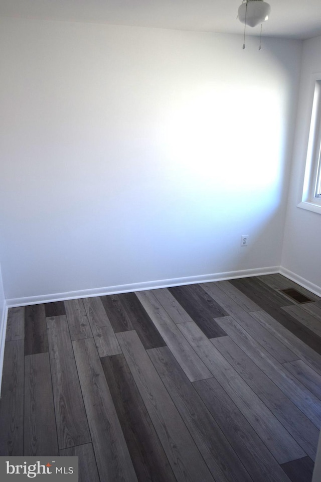 empty room featuring visible vents, baseboards, and dark wood-style flooring