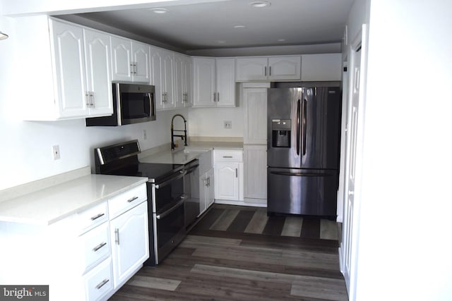 kitchen with stainless steel appliances, light countertops, dark wood-type flooring, white cabinets, and a sink