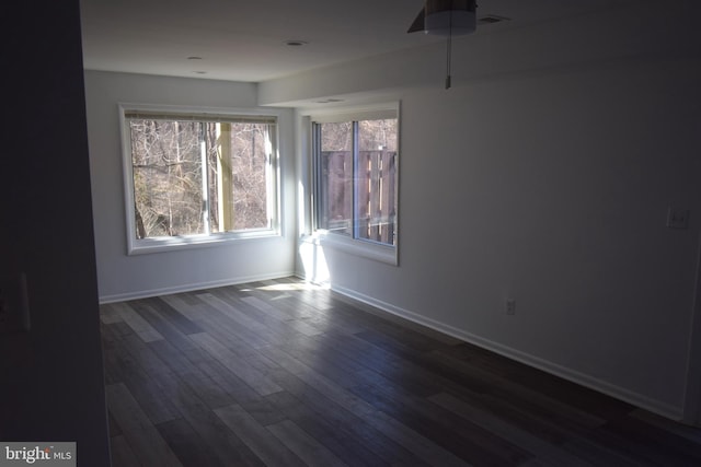 unfurnished room featuring dark wood-type flooring, visible vents, and baseboards